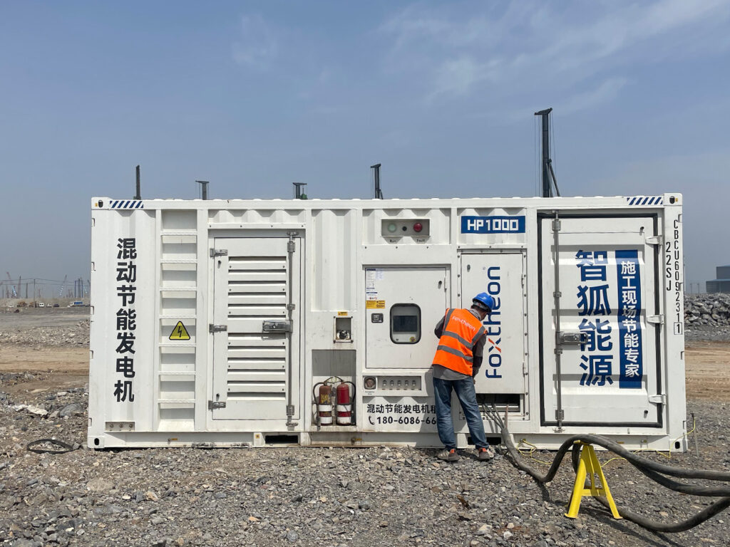 Foxtheon technician inspecting an HP1000 hybrid generator during installation at a construction site for a foundation piling project.